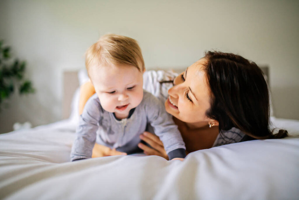 Mother and child on a white bed playing in sunny bedroom - Foto, Bild