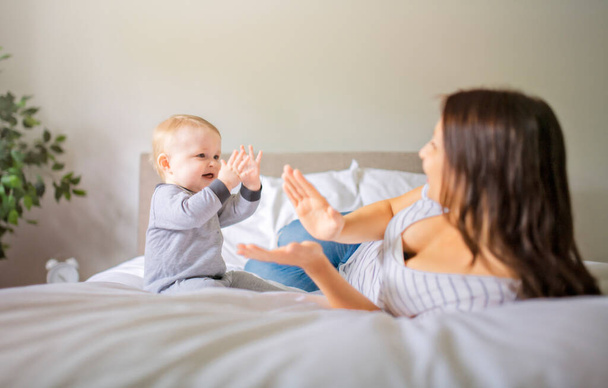 Mother and child on a white bed playing in sunny bedroom - Foto, Imagen