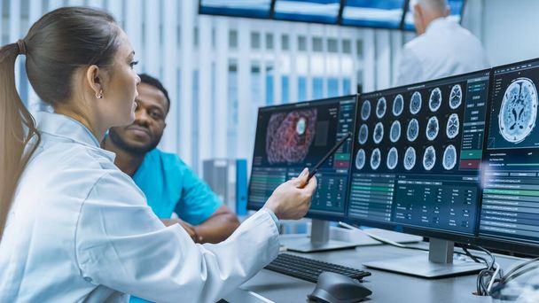 Medical Scientist and Surgeon Discussing CT Brain Scan Images on a Personal Computer in Laboratory. Neurologists Neuroscientists in Futuristic Neurological Research Center Working on a Brain Tumor - 写真・画像