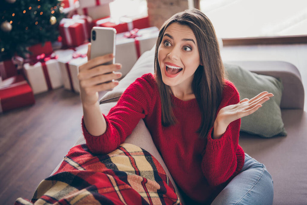 Foto von verrückten Mädchen sitzen autsch Videoanruf auf Smartphone in Haus drinnen mit Weihnachtsdekoration - Foto, Bild