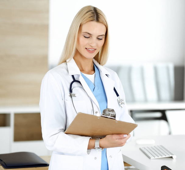 Doctor woman at work in hospital controls medication history records and exam results while using clipboard. Medicine and healthcare concept - Foto, Imagem