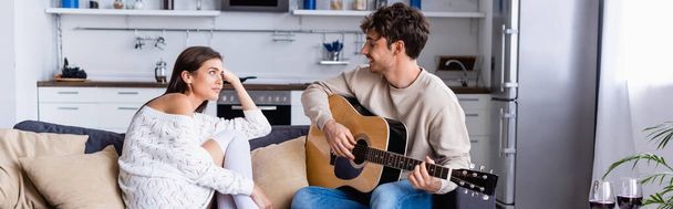 Smiling man playing acoustic guitar near girlfriend and glasses of wine at home, banner  - Фото, изображение