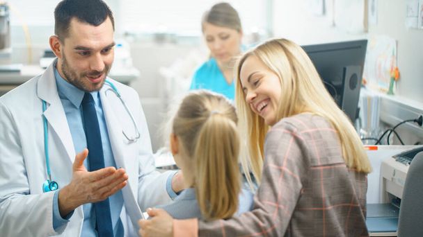 Friendly Doctor Does Routine Examination of a Sweet Little Girl who Came with Her Mother. Pediatrician Talks to Both of them. Doctors Office is Bright and Modern. - Foto, Imagem