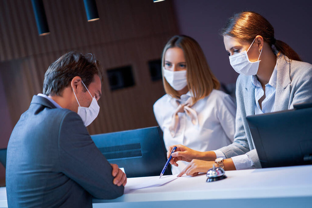 Επιχειρηματίας με μάσκα στη ρεσεψιόν ενός ξενοδοχείου check in - Φωτογραφία, εικόνα