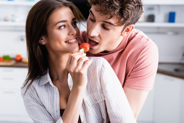Smiling woman feeding boyfriend with fresh strawberry at home  - Photo, Image