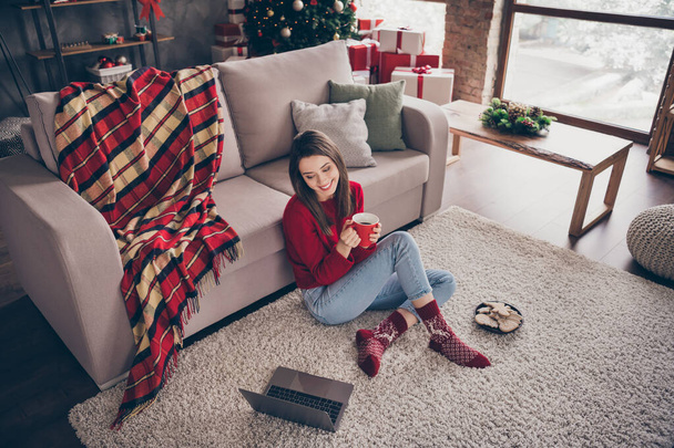 Photo of young girl sit carpet couch look screen netbook hold mug wear red sweater socks jeans in decorated x-mas living room indoors - Fotó, kép