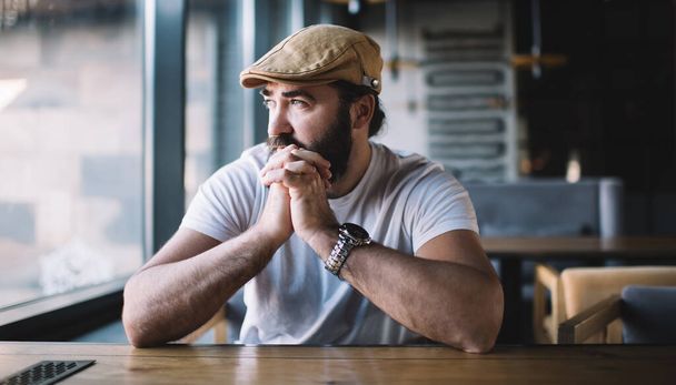 Thoughtful bearded male in casual wear looking at window in cafe pondering on ideas holding hands, serious confident handsome man 40 years spending free time in coffee shop concentrated on plans - Photo, image