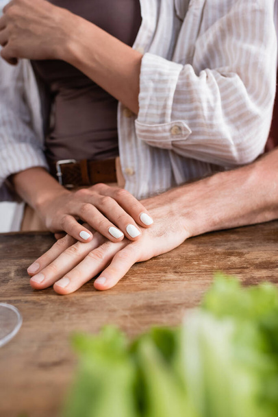Vista recortada de la mujer sosteniendo mano novio en la mesa de la cocina en primer plano borrosa  - Foto, imagen