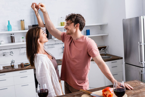 Couple dancing near paprika and wine on blurred foreground in kitchen  - Foto, Imagen