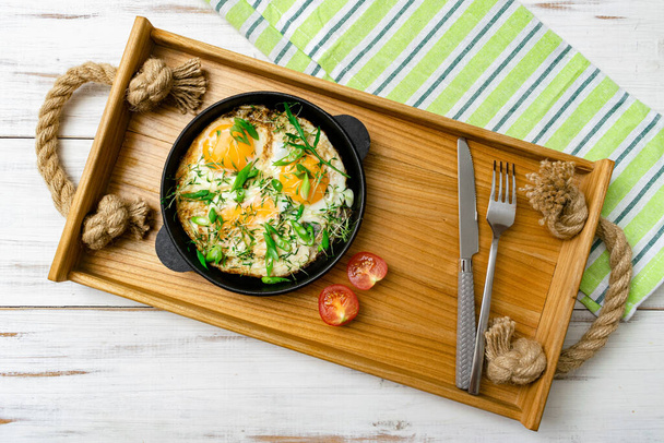 scrambled eggs with sprouts of greens and green onions in a frying pan on a wooden tray. Morning breakfast. - Foto, Imagen