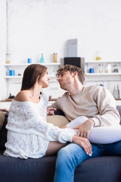 Fiatal férfi megható lábak barátnője térd zokni és kötött pulóver a nappaliban  - Fotó, kép