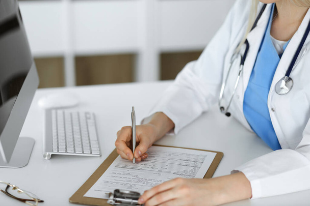 Unknown woman-doctor at work filling up medication history record form in clinic, close-up of clipboard - Foto, immagini