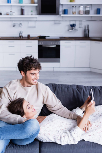 Gülümseyen çift evdeki kanepede boş ekranlı dijital tablet kullanıyor.  - Fotoğraf, Görsel