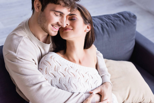 Usmívající se pár se zavřenýma očima objímající na gauči  - Fotografie, Obrázek