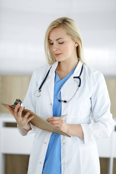 Nainen-lääkäri seisoo sairaalassa tai klinikalla ja täyttää lääkityshistorian tallennuslomakkeen. Tiedot ja paras palvelu lääketieteessä ja terveydenhuollossa - Valokuva, kuva