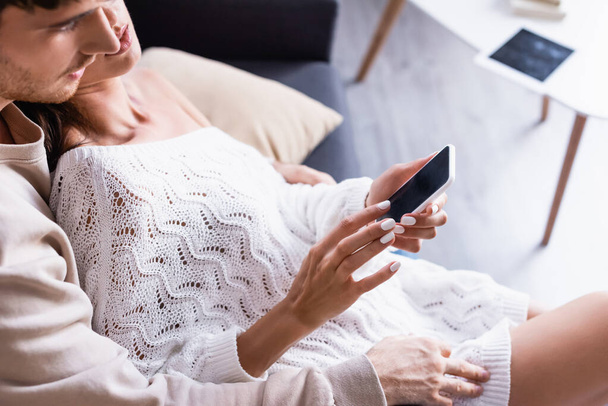 Smartphone com tela em branco em mãos de mulher perto do namorado em primeiro plano desfocado  - Foto, Imagem