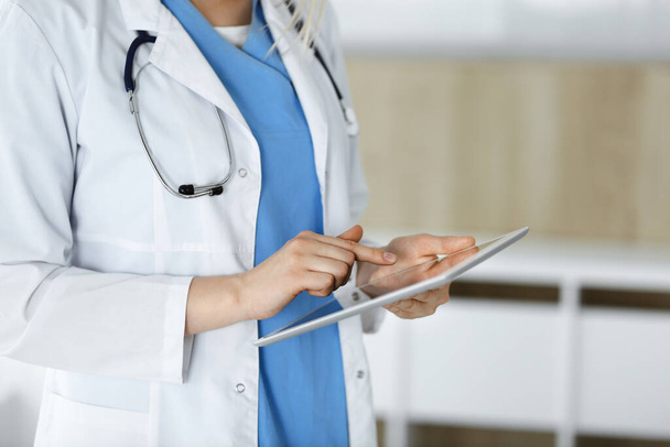 Unknown woman-doctor standing in clinic and using tablet pc, close-up. Data and best service in medicine and healthcare - Foto, Bild