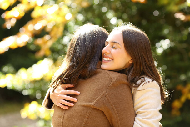 Happy friends meeting and hugging in a park in autumn season a sunny day - Fotoğraf, Görsel