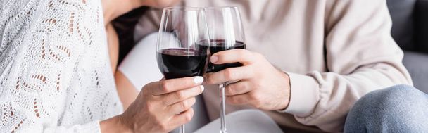 Cropped view of glasses of red wine in hands of young couple on blurred background, banner  - Foto, Imagem