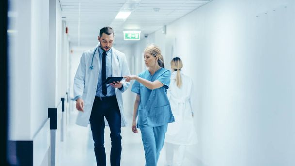 Female Surgeon and Doctor Walk Through Hospital Hallway, They Consult Digital Tablet Computer while Talking about Patients Health. Modern Bright Hospital with Professional Staff. - Fotó, kép
