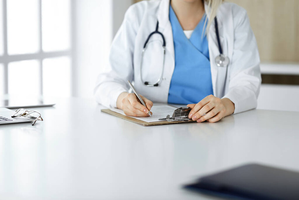 Unknown woman-doctor at work filling up medication history record form in clinic, close-up of clipboard - Foto, imagen