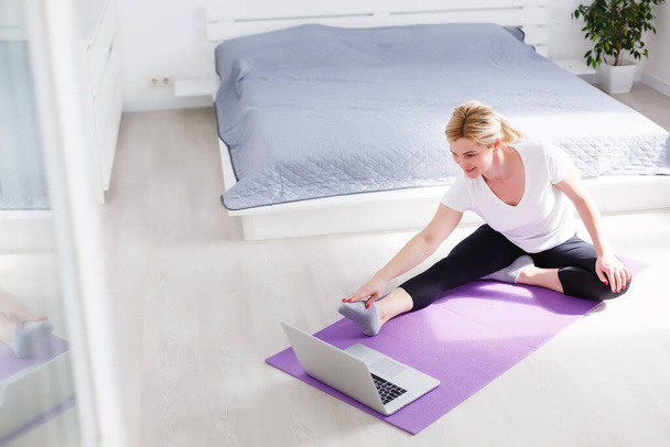 Mulher feliz fazendo exercício enquanto assiste vídeo de treino no laptop em casa - Foto, Imagem