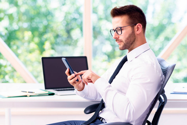 Financial businessman wearing shirt and tie while sitting at office desk and text messaging. - Photo, Image