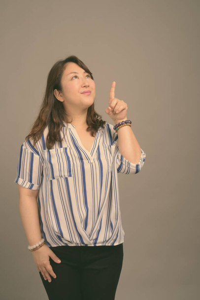volwassen mooi aziatisch zakenvrouw tegen grijs achtergrond - Foto, afbeelding