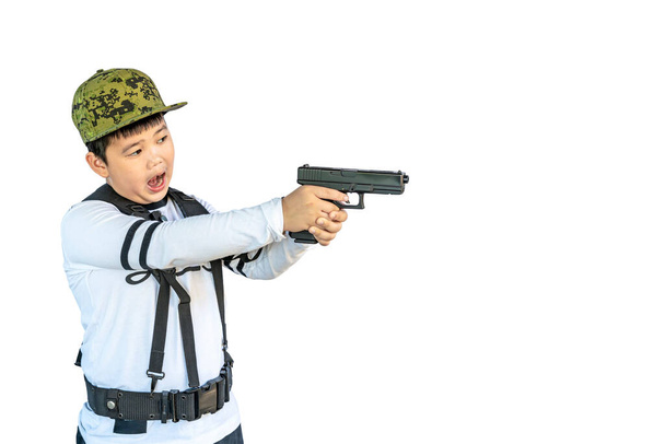 Asian boy wearing a hat and individual harness suspenders belt or military Y shoulder strap play acting self defend by aim model shooting gun isolated with clipping path - Photo, Image