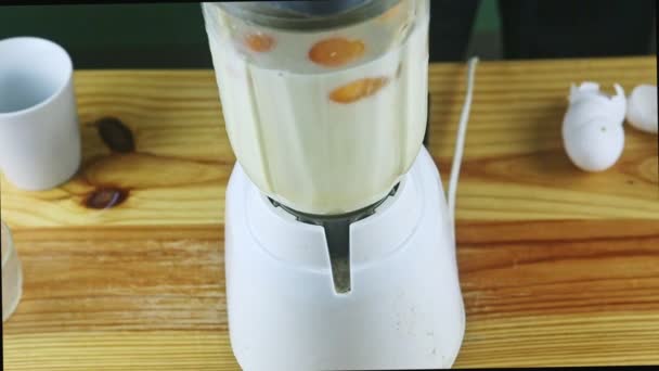 κοντινή προβολή σε ηλεκτρικό μπλέντερ ανάμειξη γάλακτος, συμπυκνωμένου γάλακτος και αυγών σε γυάλινο δισκοπότηρο - Πλάνα, βίντεο