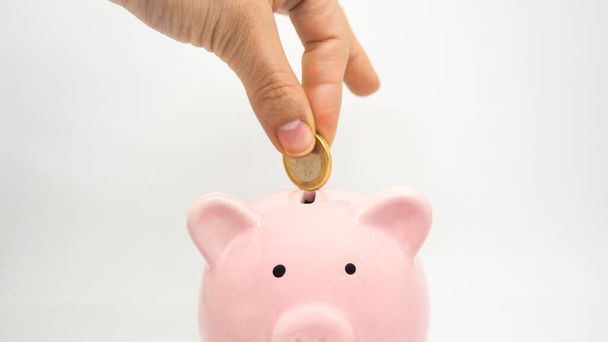Roze spaarvarken spaargeld munt op een witte achtergrond. Hand voeg munt toe aan de spaarpot. Bespaar geld, tijd, geld en business concept. - Foto, afbeelding