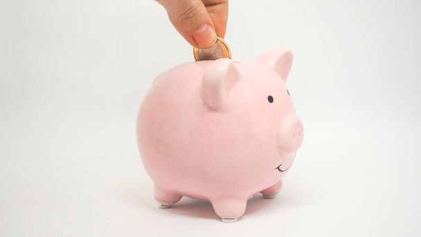 Pink piggy bank save coin on a white background. Hand add coin to piggy bank. Save coin, time, money and business concept. - Foto, afbeelding