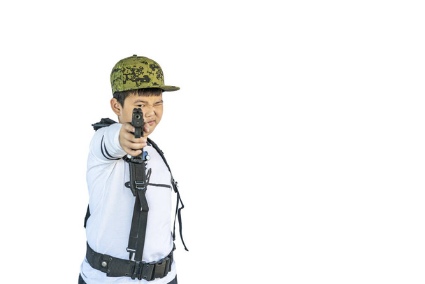 Asian boy wearing a hat and individual harness suspenders belt or military Y shoulder strap play acting self defend by aim model shooting gun isolated with clipping path - Foto, Bild