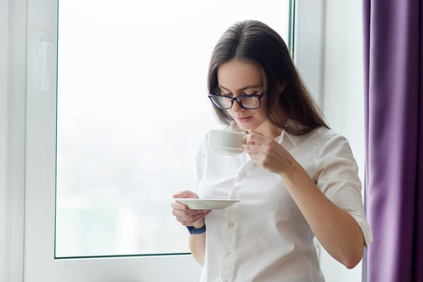 Young business woman with cup of coffee near window in office - Foto, immagini