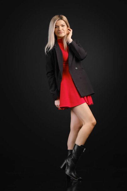 Pretty woman in red dress and black jacket posing in dark studio - Foto, afbeelding