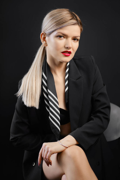 Low key portrait of woman in black jacket and scarf sitting in armchair in dark room - Fotografie, Obrázek