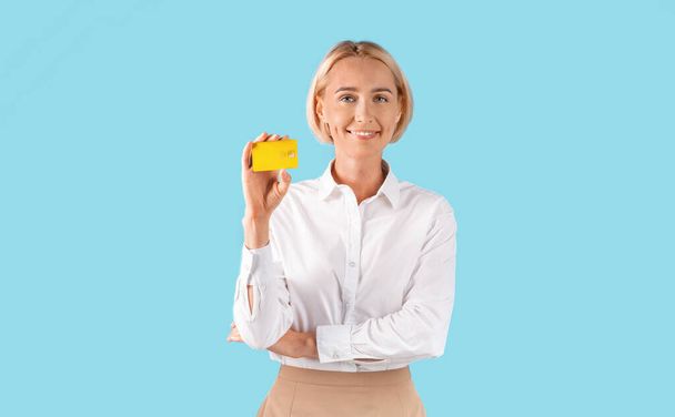 Portrait of businesswoman showing gold credit card over blue studio background, panorama - Photo, Image