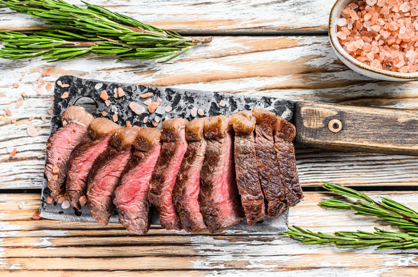 Grilled top sirloin cap or picanha steak on a meat cleaver with herbs. White wooden background. Top view. - Photo, Image