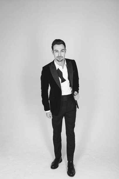 Studio portrait of a young caucasian man in a tuxedo, looking at the camera, standing against plain studio background - Foto, immagini