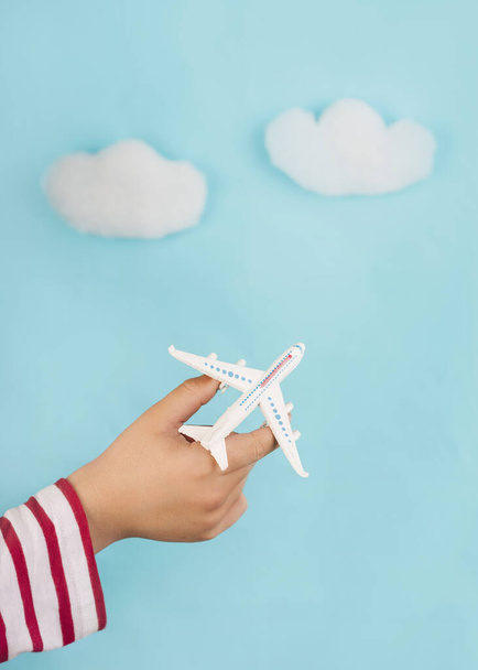 manos de niño sosteniendo un avión de juguete sobre nubes sobre fondo azul. Concepto de viaje - Foto, imagen