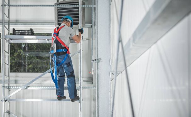 Trabajador caucásico en sus 40 años escalando en la estructura del andamio de aluminio dentro del área de trabajo. Almacén Interior. Equipo de arnés de seguridad. - Foto, imagen