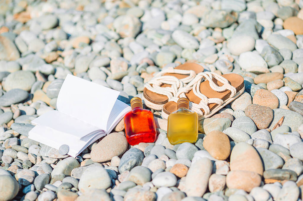 Cappello da spiaggia sul libro aperto con crema solare e scarpe sulla spiaggia di ghiaia - Foto, immagini