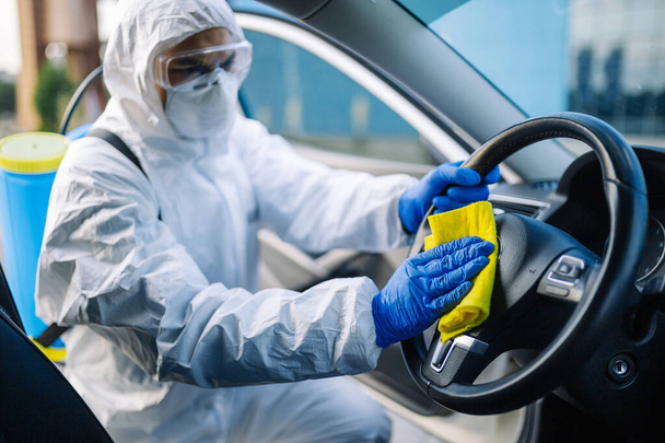 Dezenfekte uzmanı sarı halılı bir arabanın direksiyonunu temizliyor. Sağlık görevlisi, aracın sürücü koltuğunu dezenfekte eder. Covid-19 yayılmayı önlüyor. Sağlık kavramı - Fotoğraf, Görsel