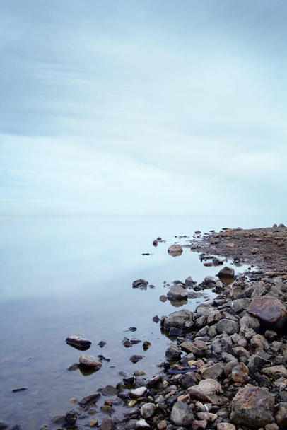 vista de um lago com céu nublado e pedras na costa - Foto, Imagem