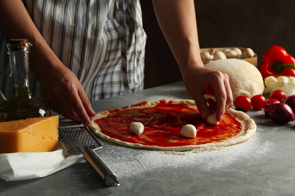 Жінка готує піцу на сірому столі з інгредієнтами
 - Фото, зображення