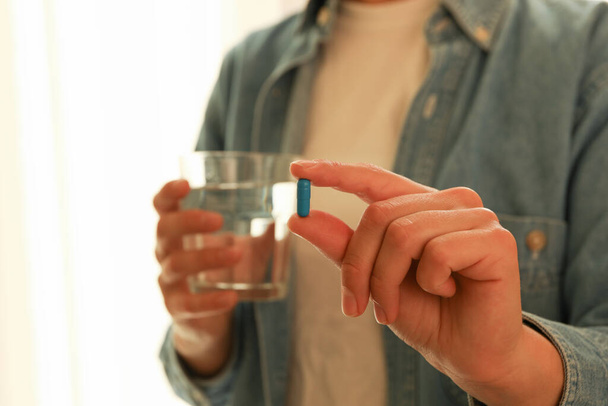 Mujer sostiene vaso de agua y cápsula de píldora azul - Foto, imagen