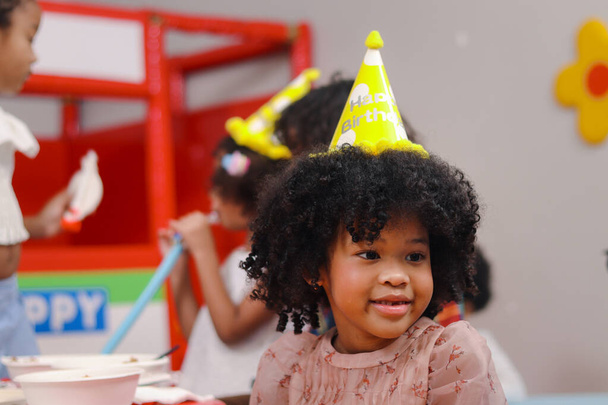 Χαρούμενο πάρτι γενεθλίων, αξιολάτρευτη Αφροαμερικανή με σγουρό καπέλο, παιδιά γιορτάζουν τα γενέθλια τους μαζί, χαρούμενα παιδιά διασκεδάζουν μαζί.. - Φωτογραφία, εικόνα