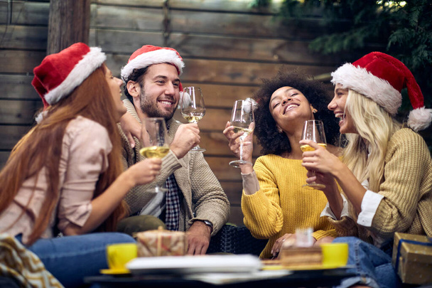 Group of young cheerful people chatting and drinking at christmas or new year party in festive atmosphere together. Xmas, friends, toast, fun, party concept - Fotografie, Obrázek