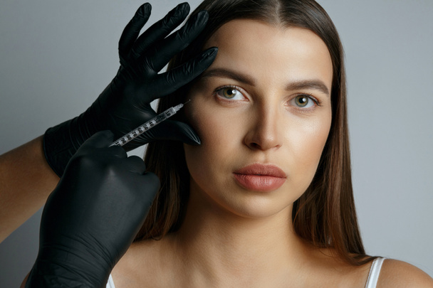 Glamouröse Frau bekommt Botox ins Gesicht gespritzt. Studioaufnahme auf grauem Hintergrund - Foto, Bild