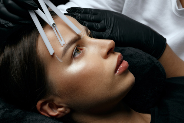 La mujer en los guantes que miden las cejas ante la tinción permanente del polvo - Foto, Imagen